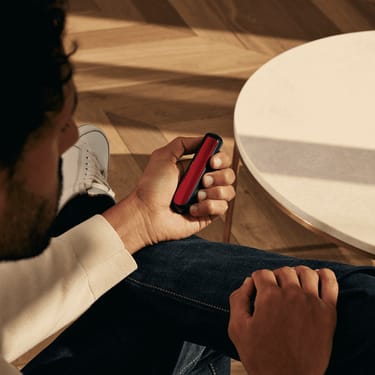 Hombre sosteniendo un dispositivo Ploom con el panel frontal Lava Red
