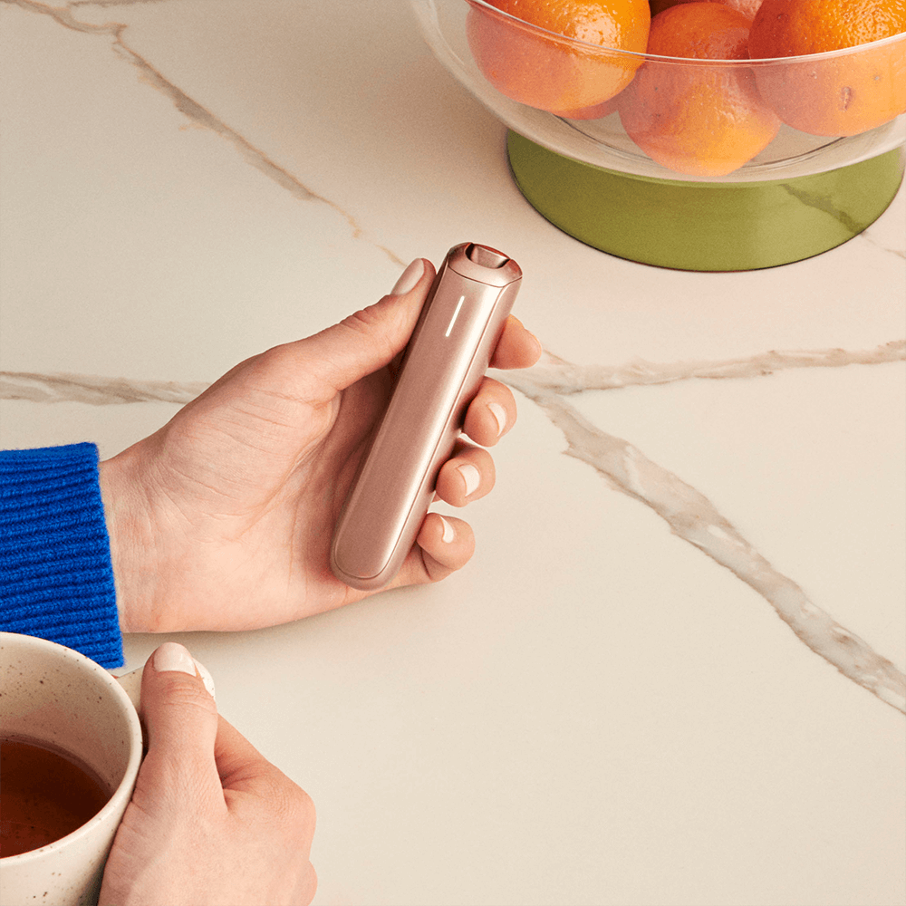 Dispositivo Ploom AURA Rose Gold sobre una mesa con té y cesta de fruta