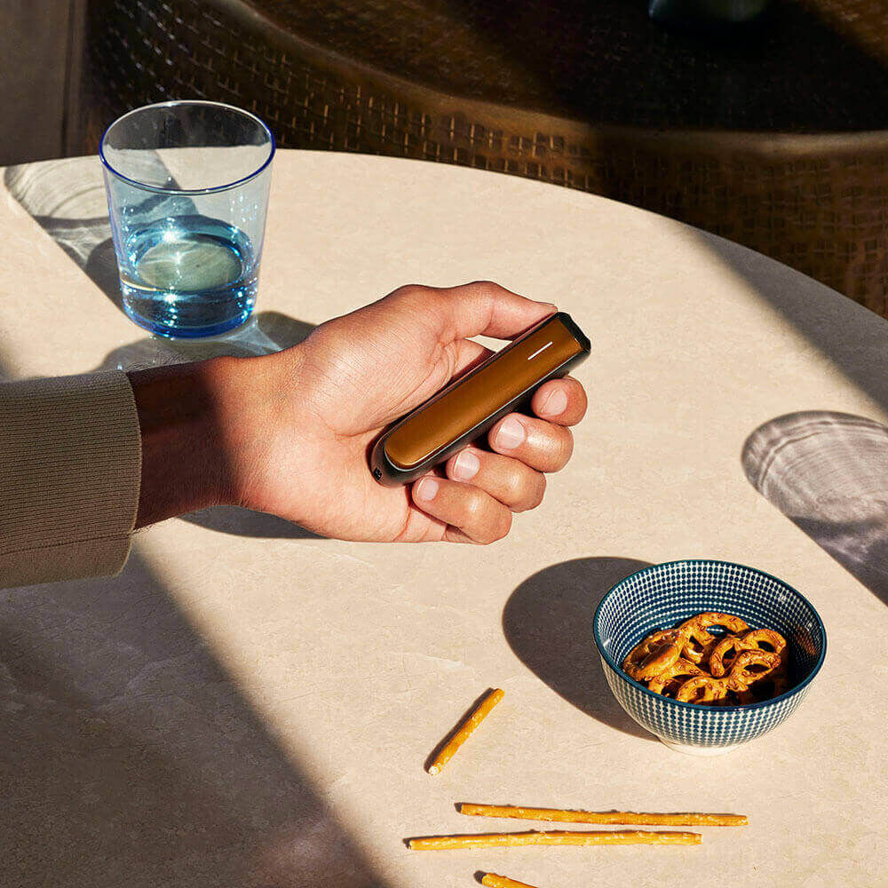 Mano sosteniendo un Ploom AURA equipado con el accesorio Panel Frontal Mango Sorbet.